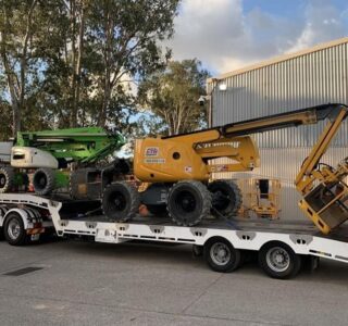 2 cherry pickers or boom lifts being transported on a low bed trailer