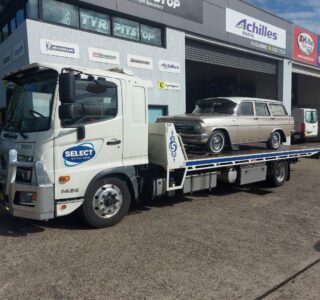 A classic Holden EJ station wagon being towed on a flat bed tow truck