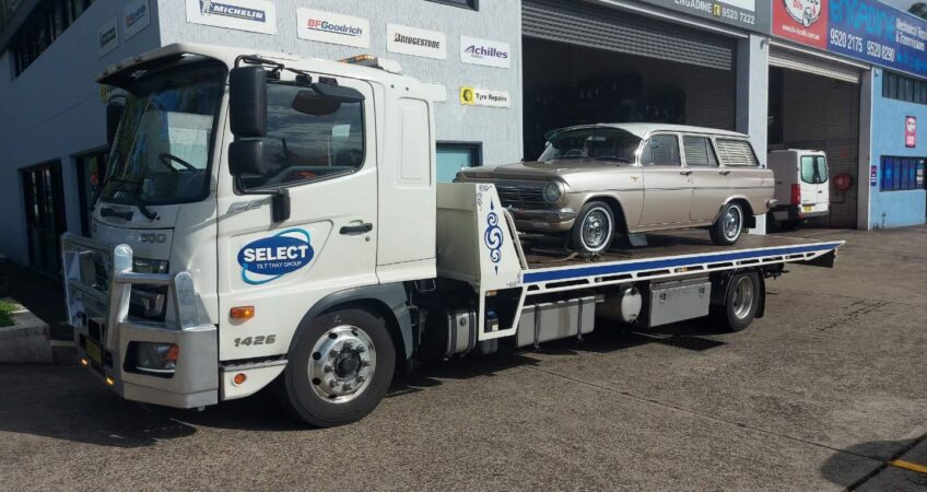 A classic Holden EJ station wagon being towed on a flat bed tow truck